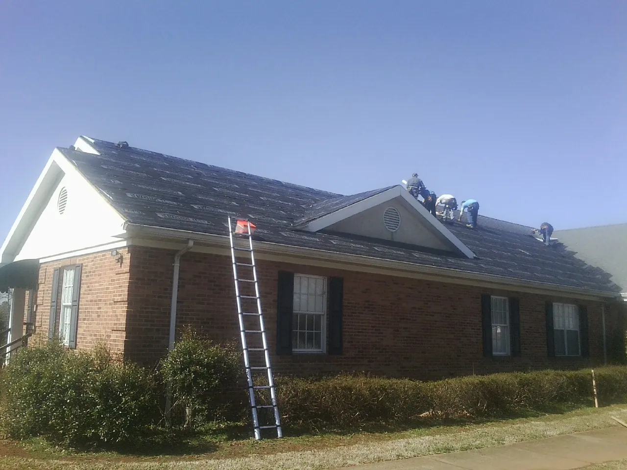 Crew tearing shingles off a brick ranch roof with a ladder set — Metal Roof Repair work by our crew in Vienna